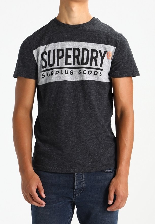 Šedé tričko s krátkým rukávem a bílým horizontálním pruhem, na kterém je text "SUPERDRY SURPLUS GOODS". Měkký bavlněný materiál, volný střih.