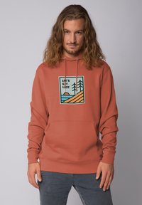 Haut à capuche couleur rouille avec une poche avant, un cordon de serrage et un design graphique mettant en avant des arbres et un soleil, fabriqué à partir d'un mélange de coton doux.