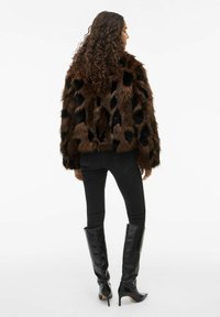 Brūns mākslīgā kažokādas mētelis ar melnu punktotu rakstu, ar strukturētu virsmu, hip-garuma dizains. Kombinēts ar melnām šaurām d žinsu biksēm un melnām zābakiem līdz ceļiem.