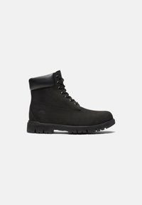 Bottes noires à cheville en daim avec un col en cuir, dotées de lacets ronds, d'une semelle en caoutchouc et d'un logo en relief sur le côté.