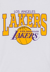 Camiseta blanca con un texto en negrita de color púrpura y amarillo que dice "LOS ANGELES LAKERS" junto a un gráfico de baloncesto, mostrando un diseño simple y directo.