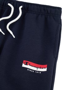 Pantalones de chándal en color navy, hechos de una tela suave, con una cinturilla elástica y cordones blancos, y un parche de logo en rojo y blanco.
