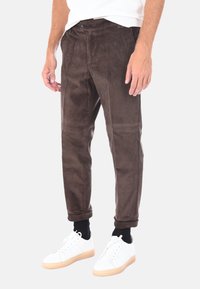 Pantaloni in corduroy marrone con strisce verticali, dotati di vita con bottone e caviglie affusolate, indossati con sneaker bianche e calzini neri.