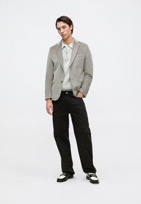 Lys grå kordfløyelsblazer over en lys genser, kombinert med svarte bukser og svarte sko med hvite detaljer. Enkel, strukturert silhuett.