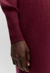 Bordeaux ribbelbreisel met een gestructureerde afwerking, met een close-up van een hand die tegen het materiaal rust.