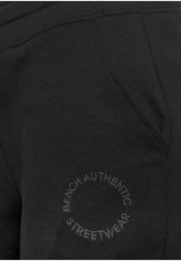 Schwarze Sweatpants mit einer seitlichen Tasche und einem runden, gestickten Design, das "BENCH AUTHENTIC STREETWEAR" in passender Farbe zeigt.