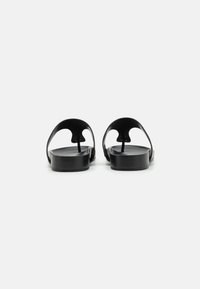 Sandali neri dal design minimalista, con due cinghie curve, suole piatte e una finitura liscia. Nessun logo o motivo visibile.