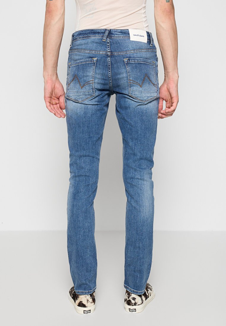 Wąskie niebieskie dżinsy o wyblakłym wykończeniu, z dwoma tylnymi kieszeniami i charakterystycznym ściegiem w zygzak. Widoczna metka na pasku.