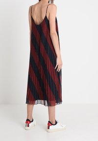 Plisserad maxiklänning med djup rygg, med diagonala marinblå och vinröda ränder. Matchas med vita sneakers med röda och blå detaljer.