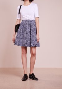 Top bianco a maniche corte abbinato a una gonna plissettata blu navy con un motivo a pois bianchi. Scarpe nere con dettagli borchiati completano l'outfit.