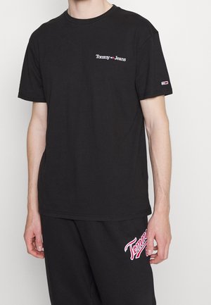T-shirt en coton noir à manches courtes, arborant un petit logo "Tommy Jeans" rouge et blanc sur la poitrine et un patch de logo sur la manche.