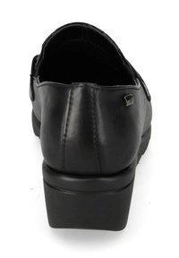 Scarpa di pelle nera con tacco basso, parte posteriore arrotondata e decorazione metallica sul lato. Texture liscia con dettagli di cucitura visibili.