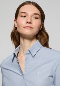 Camicia button-up a scacchi blu chiaro, realizzata in cotone, con colletto a punta, ricamo del logo discreto e texture liscia.