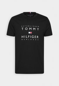 Černé bavlněné tričko s výrazným bílým textem: "ZALOŽENO TOMMY HILFIGER" a malým barevným logem uprostřed. Zaoblený výstřih.