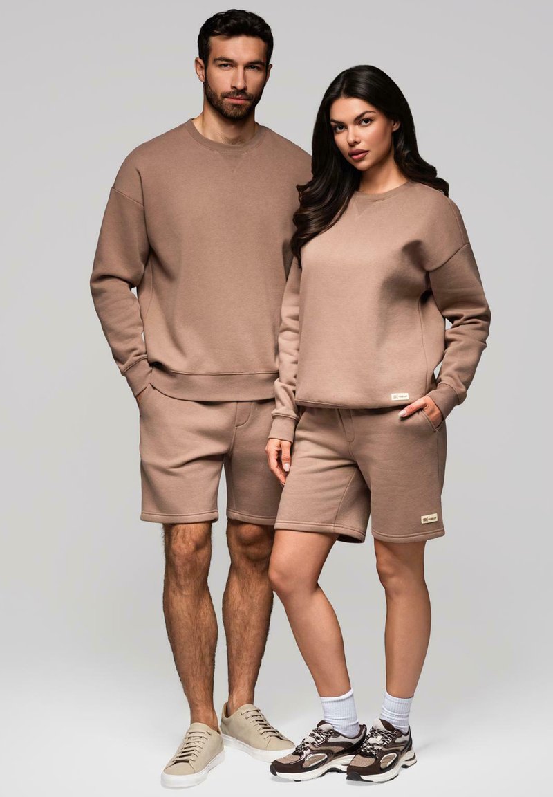 Ensemble en coton mélangé marron composé d'un sweat-shirt et d'un short. Design simple, coupe décontractée, poignets côtelés et accents de logo subtils. Porté avec des baskets neutres.
