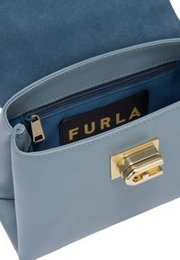 Jasnoniebieska skórzana torebka na ramię z złotym zapięciem. Wewnątrz ma niebieską podszewkę oraz kieszonkę na kartę z nazwą marki "Furla."