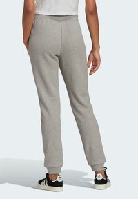 Grå sweatpants med en tapered design, elastisk midjeband och avslutade anklar. Modellen har på sig svarta och vita sneakers.