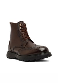 Brązowy skórzany botek za kostkę z detalami w stylu brogue, sznurowany przód i mosiężne oczka. Teksturowane wykończenie i gruba gumowa podeszwa zapewniająca przyczepność.