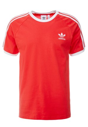 Czerwona koszulka Adidas z krótkim rękawem, białymi wykończeniami na kołnierzu i mankietach, trzema białymi paskami na ramionach oraz logo Adidas na lewej piersi.