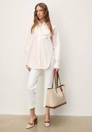 Chemise rose clair à manches longues avec fermeture à boutons ; pantalon blanc raccourci ; sac fourre-tout beige avec anses marron ; escarpins slingback crème et marron.