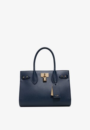 Borsa a mano in pelle blu navy con due manici, chiusura e borchie in tonalità oro, e una targhetta del marchio ALDO appesa su sfondo bianco.