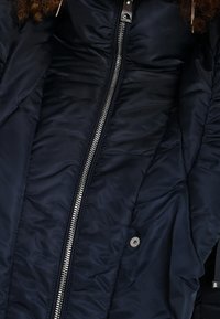 Marinblå puffjacka med en quiltad textur, med en framdragkedja, tryckknappar och elastiska ärmmuddar för extra värme och passform.