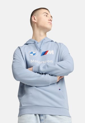 Svetlo modrá mikina s kapucňou vyrobená z mäkkej látky. Obsahuje logo a grafiku BMW Motorsport v bielej a červenej farbe. Na prednej strane sa nachádza klokaní vrecko.