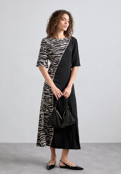 Rochie neagră cu model zebra, cu mâneci scurte și fenta diagonală. Complementată de o geantă neagră cu sclipici și pantofi negri fără toc.