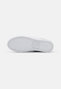 Semelle de chaussure en caoutchouc blanc texturé avec un logo en relief au centre. Bord lisse et détails à motifs tout au long.