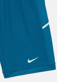 Shorts de sport teal en tissu maillé respirant. Présentent une texture lisse et un logo Nike bleu clair sur l'ourlet inférieur.