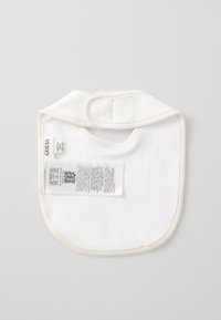 White cotton bib with a rounded shape, soft texture, and a Velcro closure at the neck. Includes a care label with printed information.