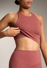 Sutien sport de culoare roz, realizat din material elastic, având un guler înalt și un design ajustat, fiind ajustat ușor.