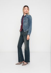 Jeansjakke i lysvask med to brystlommer, parret med en maroon topp og mørke vide jeans, komplementert av grå spisse hæler.