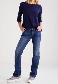 Maglietta a maniche lunghe blu navy abbinata a jeans blu chiaro. I jeans sono a gamba dritta con un effetto sbiadito, indossati con sneakers grigio chiaro.