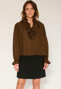 Blouse à rayures marron et noires avec un col et des poignets volantés, associée à une jupe noire, créant un effet superposé.