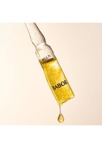 Klar glasampull med gyllene vätska inuti, märkt "MULTI VITAMIN" och "BABOR," med en droppe som bildas i botten.