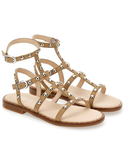 Sandalias planas de tiras en tono beige con acentos de tachuelas plateadas, suela plana y correas en el tobillo ajustables. Fabricadas con material texturizado y plantilla suave.