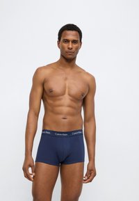 Calzoncillos tipo bóxer de algodón azul marino con una cintura con logo, de diseño ajustado y textura suave, modelados por una persona sin camiseta.