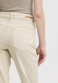 Jeans in denim beige con una vestibilità aderente, dotati di due tasche posteriori e un'etichetta in pelle sul cinturino. Tessuto semplice, hardware minimal.