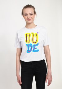 Bílý bavlněný tričko s barevným grafickým textem, který zní "DUDE" v žluté, růžové a modré barvě. Tričko má krátké rukávy a kulatý výstřih.