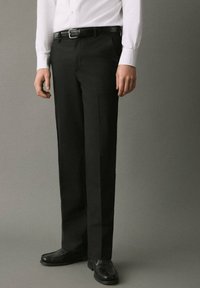 Pantalones de vestir negros hechos de una tela suave, de corte ajustado, piernas rectas, con bolsillos laterales, combinados con zapatos negros y una camisa blanca de botones.