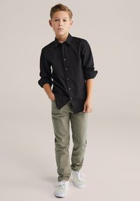 Melna garām piedurknēm krekls ar pogām, gaisīgi olīvu zaļas krāsas bikses un baltas sporta kurpes. Gluda auduma, ar uzlocītām piedurknēm un brīva piegriezuma.