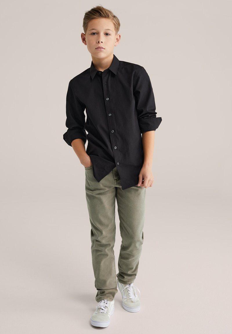 Melna garām piedurknēm krekls ar pogām, gaisīgi olīvu zaļas krāsas bikses un baltas sporta kurpes. Gluda auduma, ar uzlocītām piedurknēm un brīva piegriezuma.