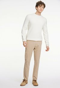 White knit sweater, beige trousers, and beige shoes. The sweater has a round neckline and long sleeves; the trousers are straight-leg.