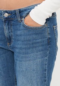 Zili denim džinsi ar klasisku piecu kabatu dizainu, ar pogu aizdari un smalku izbalēšanu. Audumam ir gluda tekstūra.