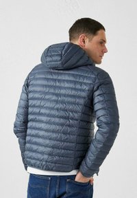 Donkerblauwe pufferjack met capuchon, met gekitte panelen en een gladde textuur. Het ontwerp is aansluitend en lichtgewicht, geschikt voor het dragen in lagen.