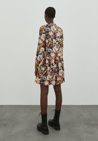 Bloemjurk in multicolore patronen met lange mouwen, cinched taille en vloeiende rok; gedragen met zwarte combatlaarzen.