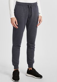 Mörkgrå joggingbyxor med dragsko i midjan, smalnade anklar och en mjuk textur, tillsammans med svarta sportskor.