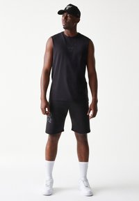 Μαύρο αμάνικο τοπ με διακριτικό λογότυπο ταύρου, συνδυασμένο με μαύρο σορτς που έχει σχέδιο στο πλάι. Λευκές κάλτσες και αθλητικά παπούτσια ολοκληρώνουν την εμφάνιση.