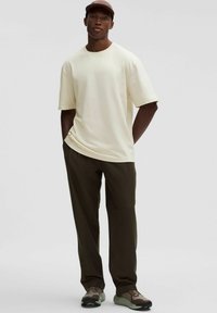 Svetlá krémová tričko s krátkym rukávom, vo voľnom strihu. Skombinované s tmavozelenými nohavicami a hnedými teniskami s zelenými akcentmi. Neformálny outfit.